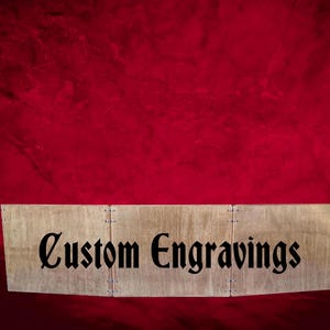 May include: A wooden sign with the text "Custom Engravings" in black lettering. The sign is made of three pieces of wood and has a natural wood finish.