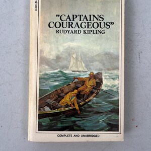May include: Vintage paperback book titled "CAPTAINS COURAGEOUS" by Rudyard Kipling. The cover art depicts a boat with two people in yellow coats on rough seas, a sailboat in the distance, and the text "LARGER TYPE FOR EASY READING".
