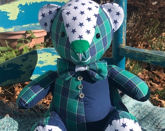 Pode incluir: Um urso de peluche xadrez verde e azul com estrelas brancas nas orelhas e pés. O urso está usando uma gravata borboleta azul e tem um nariz verde.