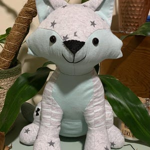May include: A light blue and gray plush fox toy with black eyes and a black nose. The fox has a striped pattern on its legs and stars on its body.