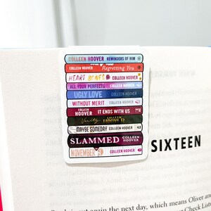 May include: A stack of colourful book spine stickers featuring the titles of Colleen Hoover novels, including "Reminders of Him", "Regretting You", "Heart Bones", "All Your Perfects", "Ugly Love", "Without Merit", "It Ends With Us", "Verity", "Maybe Someday", "Slammed", and "November 9". The stickers are arranged in a stack, with the titles facing outwards. The word "SIXTEEN" is visible on the page behind the stickers.