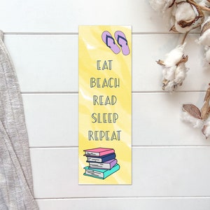 May include: Yellow bookmark with a watercolor effect featuring a stack of books, flip flops, and the text "Eat Beach Read Sleep Repeat".