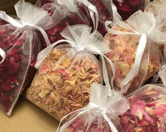 May include: A box filled with small white organza bags containing dried rose petals. The bags are tied with white ribbon and the petals are a mix of pink and peach.