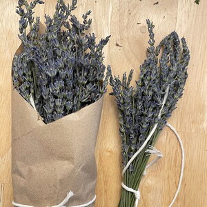 May include: Two bundles of lavender flowers, one wrapped in brown paper and tied with twine, the other tied with twine on a wooden surface.