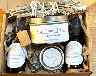 May include: A gift box filled with a variety of items, including a white sage smudge stick, a small tin of "Yucca Santa Fe" incense, a bottle of "Rosemary Sage Room Spray", a bottle of "Sandalwood Room Spray", a small glass bottle filled with colorful crystals, and a tin labeled "Girl Gone Herbal Modern Hippie".