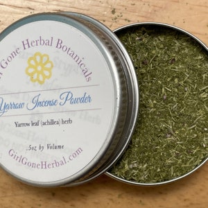 Peut inclure: Une petite boîte en métal avec une étiquette blanche qui indique "Girl Gone Herbal Botanicals Yarrow Incense Powder Yarrow leaf (achillea) herb .5oz by Volume GirlGoneHerbal.com". La boîte est ouverte et remplie d'herbe de yarrow verte séchée.