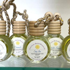 May include: Five glass bottles with wooden stoppers and string hangers. Each bottle contains a different essential oil blend. The labels are white with black text and a yellow flower graphic. The labels read: Lemon Lover, Creamsicle, Spicy Lime, Lavender Lemonade, and Peppermint Lemonade.