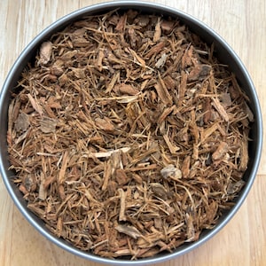 May include: A close-up of a metal container filled with brown wood chips. The chips are thin and fibrous, and they appear to be made from bark or twigs.