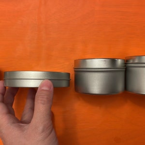 May include: Four silver metal tins of varying sizes. The tins are round and have a smooth, shiny finish.