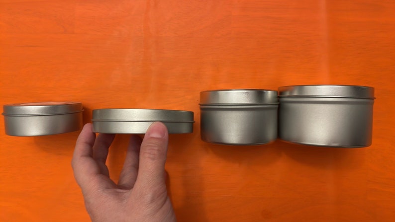 May include: Four silver metal tins of varying sizes. The tins are round and have a smooth, shiny finish.