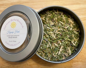 May include: A silver tin with a clear lid containing dried hyssop herb. The label on the tin reads "Girl Gone Herbal Botanicals Hyssop Herb Certified organic hyssop herb (Hysopus officinalis) 2oz by Volume GirlGoneHerbal.com".