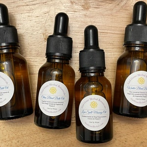 Może przedstawiać: Cztery małe, bursztynowe butelki ze szklanymi kroplomierzami, każda z inną mieszanką olejków eterycznych. Etykiety są białe z czarnym tekstem i przedstawiają kwiatowy wzór. Etykiety zawierają napis "Girl Gone Herbal Botanicals" i wymieniają nazwę każdej mieszanki: "Winter Blend Bath Oil", "Citrus Blend Bath Oil", "Love Spell Massage Oil" i "Sleepy Day Bath Oil".