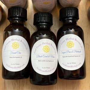 Puede incluir: Tres pequeños frascos de vidrio marrón con tapas negras y etiquetas blancas. Las etiquetas tienen un diseño de flor amarilla y texto que dice "Girl Gone Herbal Botanicals" y el nombre del aceite de fragancia. Las fragancias son "Forest Chai", "Black Coral & Moss" y "Sugar Pine & Patchouli".
