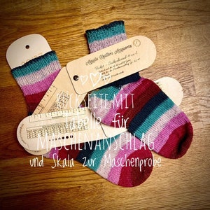 May include: Two pairs of colorful striped socks with a wooden ruler and a card that says "Ayala Guller's Memories Ficket - Sockenbancal 4-ra-1" with a heart symbol. The ruler has a scale for measuring stitches and a table for calculating stitch size.