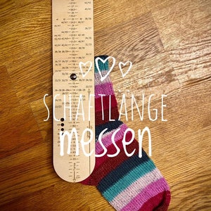 May include: A wooden sock measuring tool with a ruler in centimeters and inches. The tool is labeled "SCHAFTLANGE messen" which translates to "Measure the shaft length". A colorful striped sock is next to the tool.