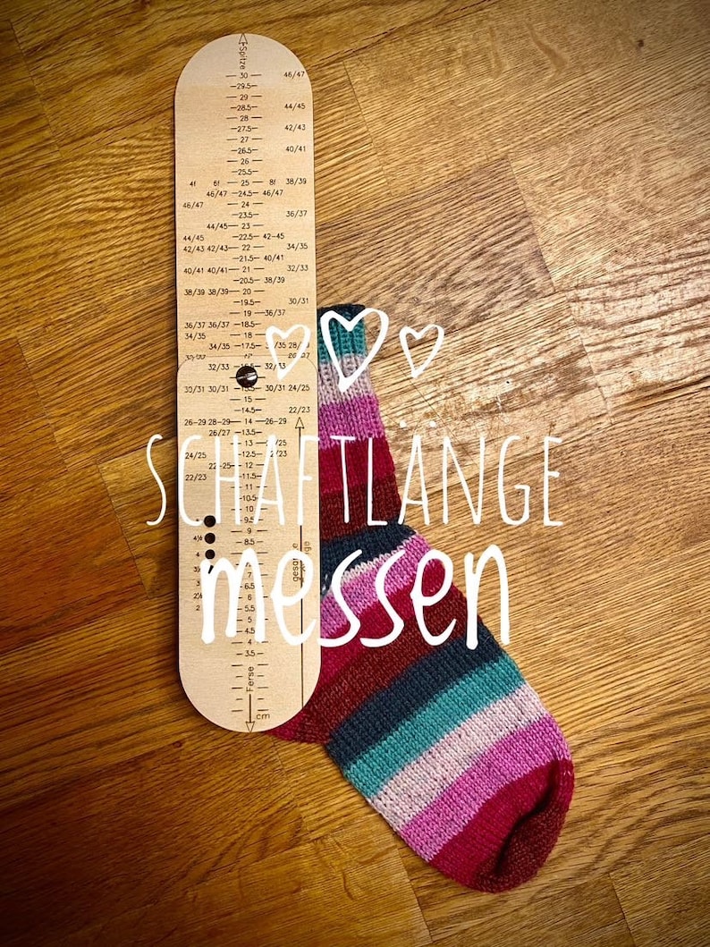 May include: A wooden sock measuring tool with a ruler in centimeters and inches. The tool is labeled "SCHAFTLANGE messen" which translates to "Measure the shaft length". A colorful striped sock is next to the tool.