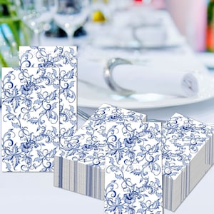 May include: A stack of white paper napkins with a blue floral pattern. The napkins are folded and stacked on a white surface.