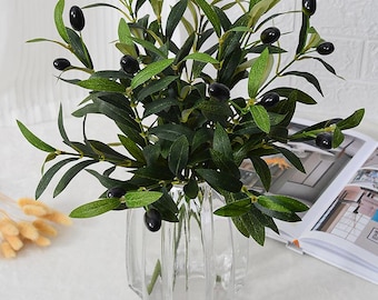 May include: A bouquet of artificial olive branches with black olives arranged in a clear glass vase. The vase has a ribbed design.