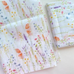 May include: White fabric with a watercolor floral pattern featuring orange poppies, purple lavender, and other wildflowers. The design includes green stems and leaves, with yellow and blue accents. The fabric is folded and appears to be a textile.