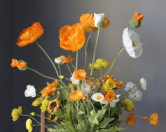 May include: A bouquet of orange and white poppy flowers with yellow sunflower accents. The flowers are arranged in a vase and are in full bloom.