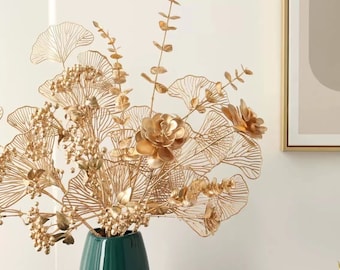 Könnte beinhalten: Eine goldene Blumenarrangements aus Metall mit zarten Blättern und Blüten in einer dunkelgrünen Vase. Das Arrangement zeigt ein Ginkgoblatt-Design und ist perfekt, um jedem Raum einen Hauch von Eleganz zu verleihen.