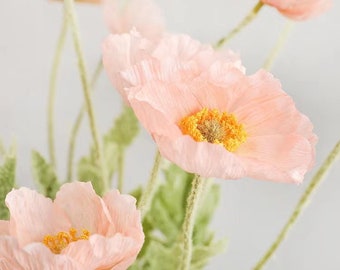 May include: A bouquet of delicate pink paper poppies with yellow centers. The flowers are arranged in a vase and have long stems.