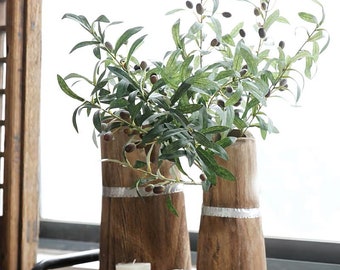 May include: Two wooden vases with a silver band around the middle, each holding a sprig of olive branches with green leaves and small black olives.