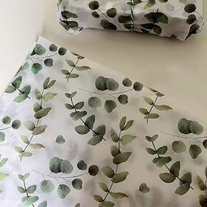 May include: White tissue paper with a watercolor eucalyptus leaf pattern. The leaves are in shades of green and gray, creating a natural and elegant design. A wrapped package is also visible.