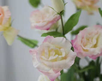 May include: A bouquet of artificial flowers with pink and white lisianthus blooms. The flowers have a delicate, layered appearance and are arranged with green stems and leaves.
