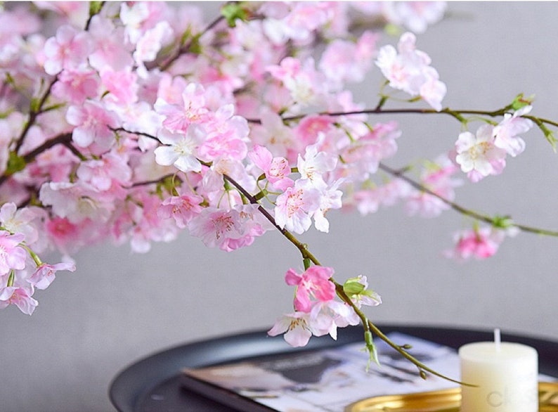 May include: A branch of delicate pink cherry blossoms with white centers. The blossoms are arranged in clusters along the branch, creating a beautiful and delicate display.