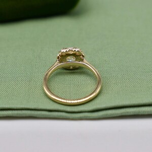 K&ouml;nnte beinhalten: Ein goldener Ring mit einem runden, klaren Stein, der in einem Heiligenschein aus kleineren Steinen gefasst ist.