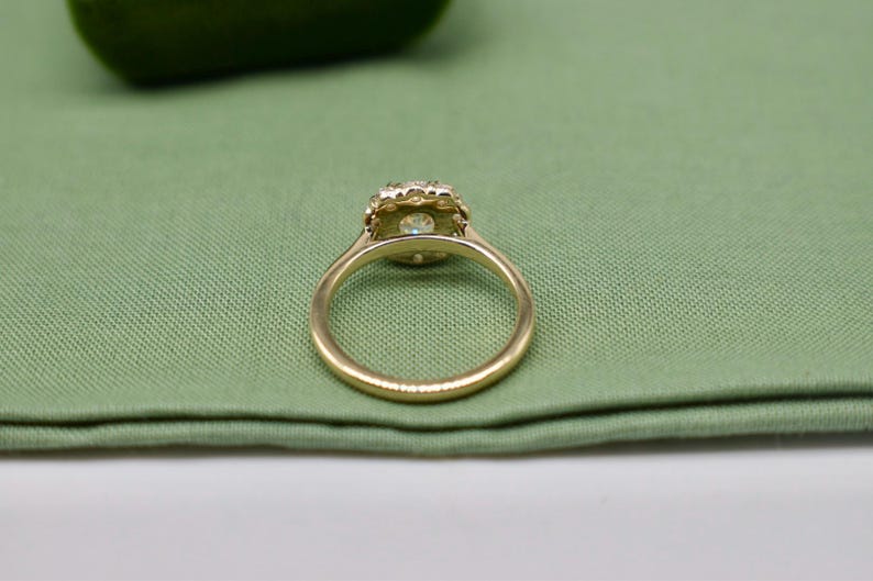 K&ouml;nnte beinhalten: Ein goldener Ring mit einem runden, klaren Stein, der in einem Heiligenschein aus kleineren Steinen gefasst ist.