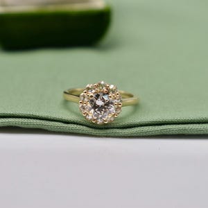 K&ouml;nnte beinhalten: Ein goldener Ring mit einem gro&szlig;en, runden, klaren Edelstein, der von kleineren Edelsteinen umgeben ist.