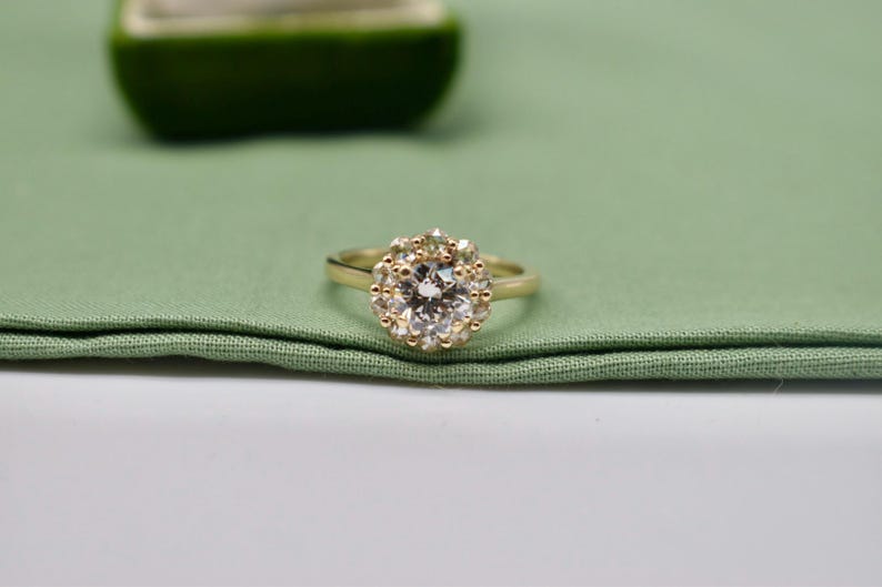 K&ouml;nnte beinhalten: Ein goldener Ring mit einem gro&szlig;en, runden, klaren Edelstein, der von kleineren Edelsteinen umgeben ist.