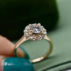 K&ouml;nnte beinhalten: Ein goldener Ring mit einem gro&szlig;en runden Diamanten, der von einem Heiligenschein aus kleineren Diamanten umgeben ist.