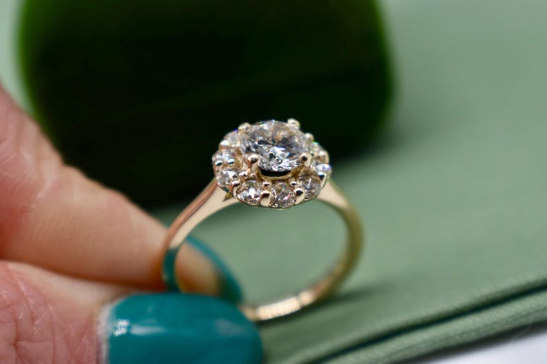 K&ouml;nnte beinhalten: Ein goldener Ring mit einem gro&szlig;en runden Diamanten, der von einem Heiligenschein aus kleineren Diamanten umgeben ist.