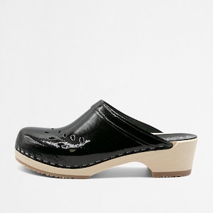 May include: Black leather clog with a wooden heel and a cutout design. The clog has a white sole.