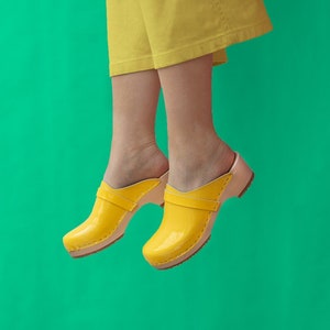 Girl wearing yellow pants and low heel clog mules in yellow leather on a light wood base