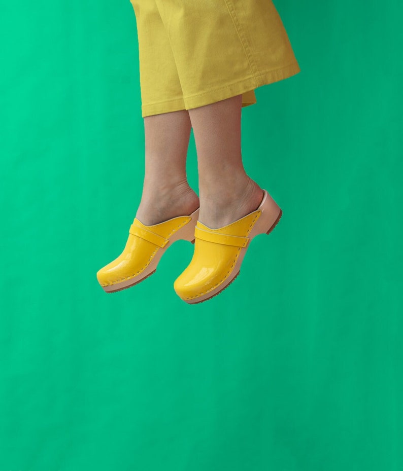 Girl wearing yellow pants and low heel clog mules in yellow leather on a light wood base