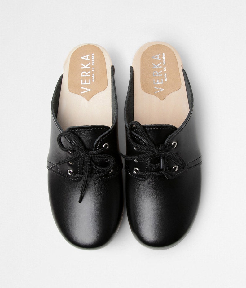 Low heel clog mules in black leather with lace on a light wood base