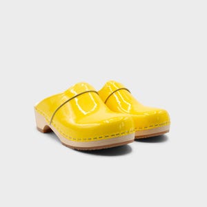 Peut inclure: Une paire de sabots jaune vif avec une finition brillante. Les sabots ont une semelle en bois et une bride sur le dessus. Les chaussures sont d'une couleur vive et ensoleill&eacute;e, parfaites pour un look d&eacute;contract&eacute; et &eacute;l&eacute;gant.