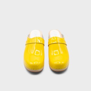 Peut inclure: Paire de sabots jaune vif avec une finition brillante. Les sabots ont une semelle en bois et une bride sur le dessus. Les sabots sont de style &agrave; enfiler et sont pr&eacute;sent&eacute;s sur fond blanc. Pointure 39.
