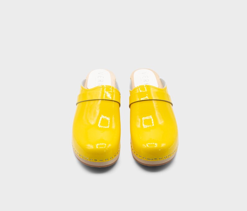 Peut inclure: Paire de sabots jaune vif avec une finition brillante. Les sabots ont une semelle en bois et une bride sur le dessus. Les sabots sont de style &agrave; enfiler et sont pr&eacute;sent&eacute;s sur fond blanc. Pointure 39.