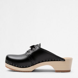 Low heel clog mules in black leather with lace on a light wood base