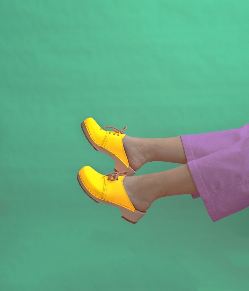 Girl wearing purple pants and low heel clog mules in yellow leather with lace on a light wood base