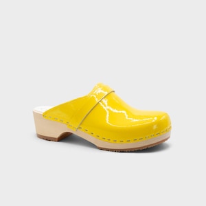 Peut inclure: Un sabot jaune unique avec une finition brillante. La chaussure a une semelle et un talon en bois, avec une bride sur le dessus. Le sabot est d'un jaune vif et ensoleill&eacute;.