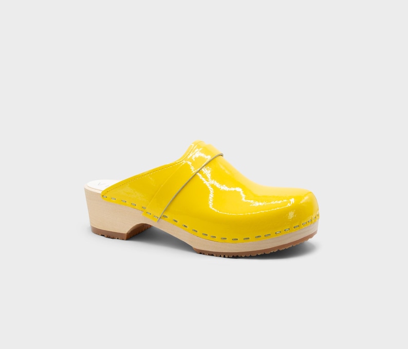 Peut inclure: Un sabot jaune unique avec une finition brillante. La chaussure a une semelle et un talon en bois, avec une bride sur le dessus. Le sabot est d'un jaune vif et ensoleill&eacute;.
