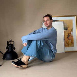 Girl wearing blue jeans and blue sweater and low heel clog mules in black leather with lace on a light wood base