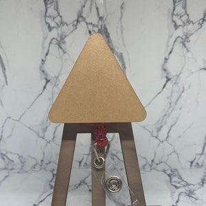 May include: A wooden easel with a triangular canvas and a clear plastic badge holder attached to the top. The easel is brown and the canvas is beige.