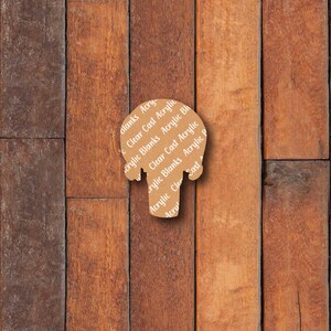 May include: A brown acrylic blank in the shape of a head, with the words "Clear Cast Acrylic Blanks" printed on it. The blank is set against a background of vertical wooden planks in varying shades of brown.